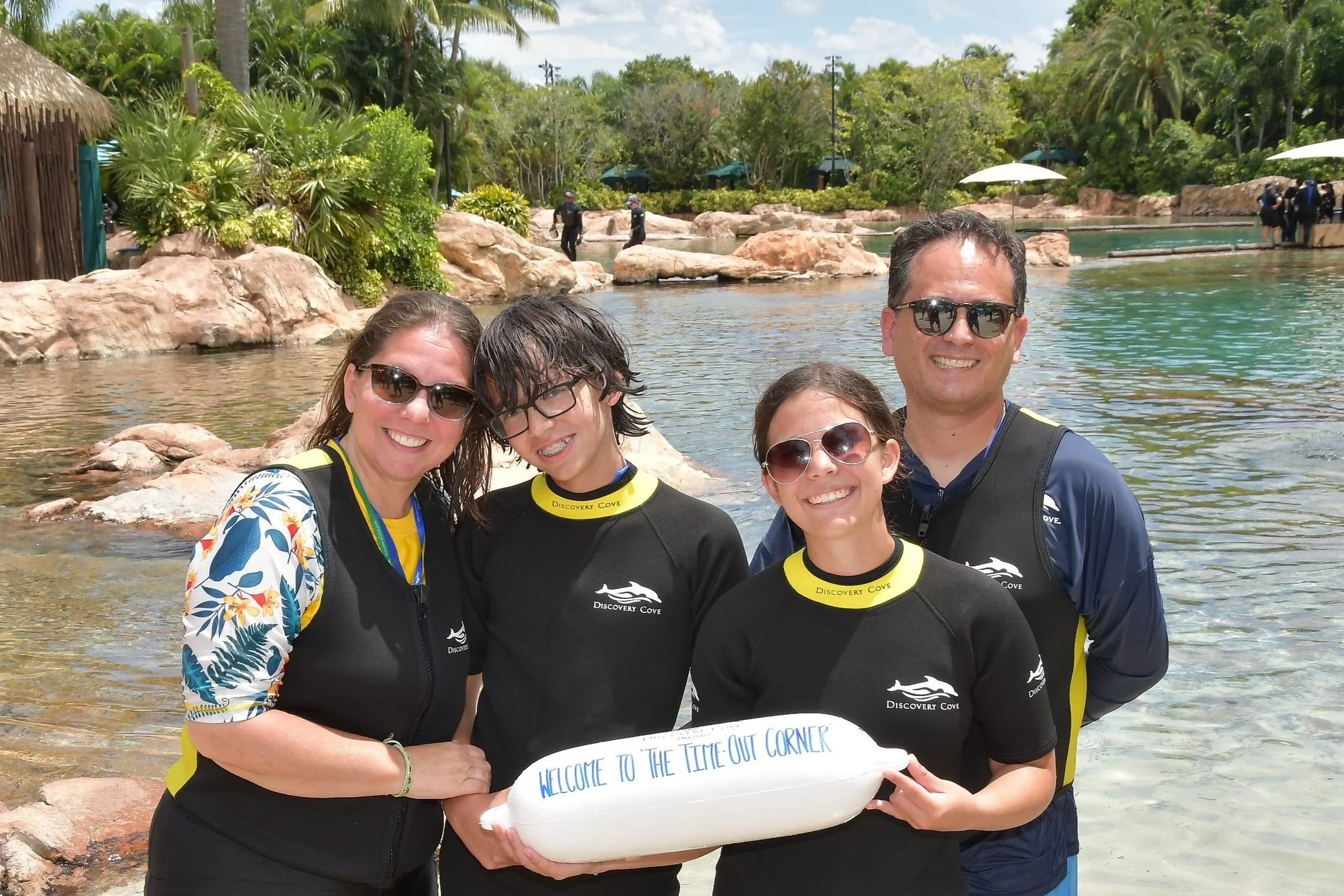 Alan and Christine with their family at Discovery Cove, holding a Welcome to The Time-Out Corner sign